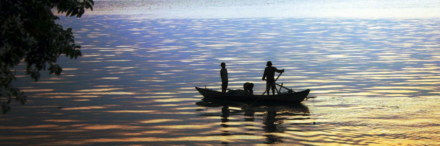 Two fishermen seen in silhouette standing in a small fishing boat at sunset